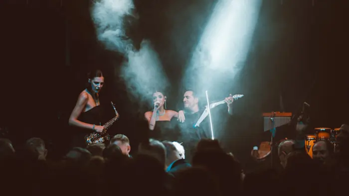 A singer performs at a packed corporate event alongside a violinist and a saxophonist | Mikevents