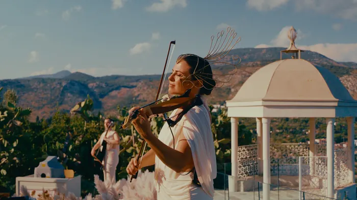Violinist in a white dress playing outdoors on a terrace with a sweeping view | Mikevents